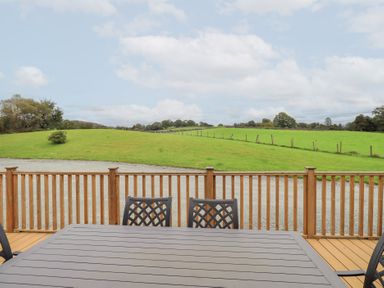 An outdoor area with a wooden table and chairs overlooking grassland at The Loghey in Hawkshead