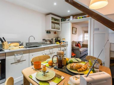 A kitchen with a wooden table set for breakfast and a couch visible through the doorway at Lettera in Ambleside