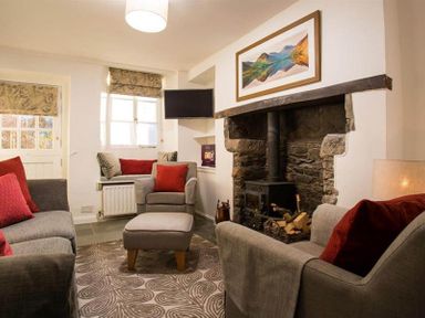 A living room with grey sofas and red cushions a wood burning stove and a wall painting at Lettera in Ambleside