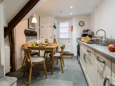 A kitchen with a wooden dining table and chairs bread on the counter and a clock on the wall at Lettera in Ambleside