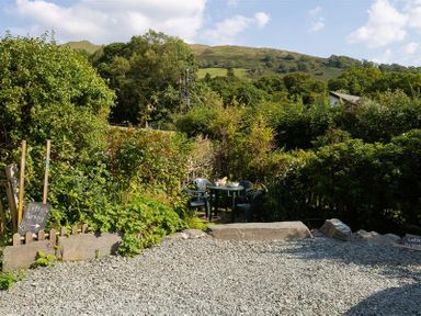 A gravel parking area with a garden and a table with chairs surrounded by greenery at Lettera in Ambleside