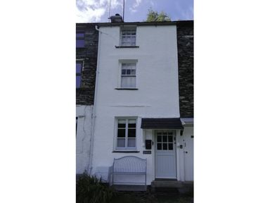 A white three-story house with two windows a door a bench and plants at Lettera in Ambleside