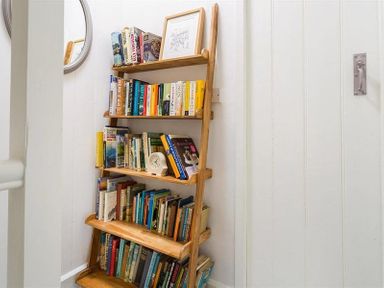 A wooden ladder bookshelf filled with books and a small clock in a hallway at Lettera in Ambleside