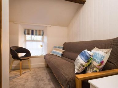 A small room with a window and striped blind a brown chair and a brown sofa with striped cushions at Lettera in Ambleside