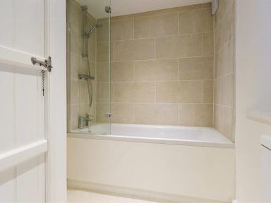 A bathroom with a bathtub shower and beige tiled walls at Lettera in Ambleside