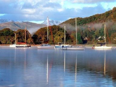 Several sailboats moored on a calm lake with forested hills and mountains in the background at Lettera Ambleside