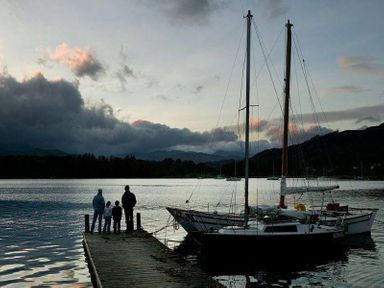 A wooden dock with four people standing on it next to two sailboats on a lake with mountains in the background at Lettera in Ambleside