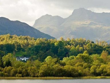 A lake with trees and a house in front of mountains at Lettera in Ambleside