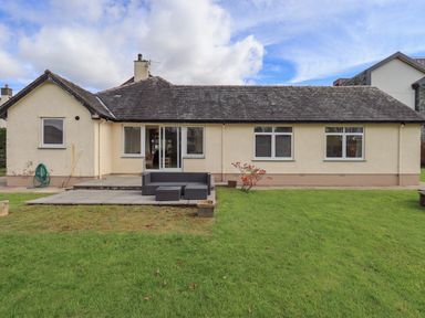 A single story house with multiple windows a patio with outdoor seating and a grassy lawn at Laal Field House in Keswick