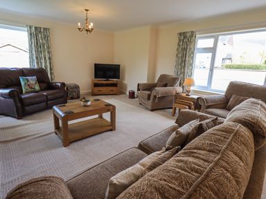 A living room with brown sofas wooden coffee table television and large windows at Laal Field House in Keswick