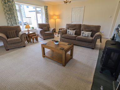 A living room with two armchairs a sofa wooden coffee table and a window at Laal Field House in Keswick