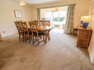 A dining room with a wooden table and chairs a sideboard with lamps and a sliding glass door with curtains at Laal Field House in Keswick