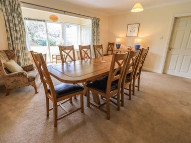 A dining room with a wooden table and chairs near glass doors and an armchair at Laal Field House in Keswick
