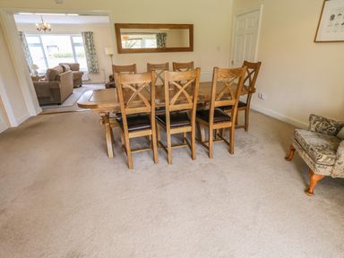 A dining room with a wooden table and eight chairs and a living room with sofas visible through a doorway at Laal Field House in Keswick