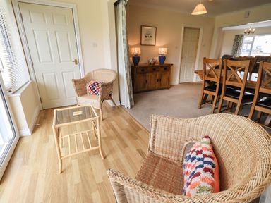 A room with wicker chairs with colorful cushions a small glass table a wooden sideboard with lamps and a dining area with wooden chairs at Laal Field House in Keswick