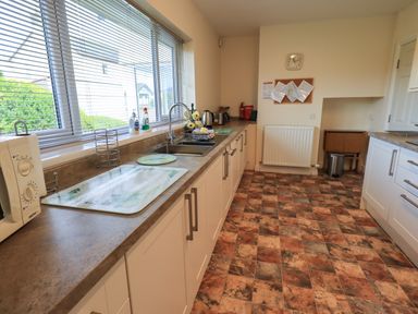 A kitchen with a large window, countertop with a sink, microwave, cutting boards, kettle, and cabinets at Laal Field House in Keswick