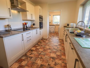 A kitchen with white cabinets a built in oven a stove and a sink with a window at Laal Field House in Keswick