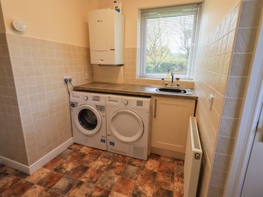 A utility room with washing machine and dryer under a countertop with a sink by a window at Laal Field House in Keswick