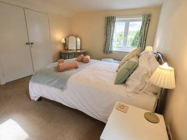 A bedroom with a bed with pillows and rolled towels bedside tables with lamps a window with curtains and a dressing table at Laal Field House in Keswick