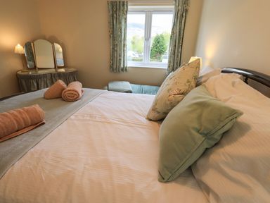 A bedroom with a bed pillows rolled towels a dressing table with three mirrors and a window with curtains at Laal Field House in Keswick