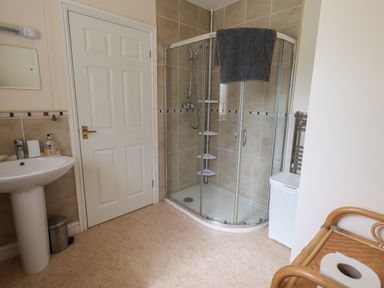A bathroom with a shower enclosure a sink a door a wicker shelf and a laundry basket at Laal Field House in Keswick