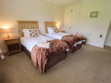 A bedroom with two single beds with brown throws and wooden headboards a wooden nightstand with lamps and a white wardrobe at Laal Field House in Keswick