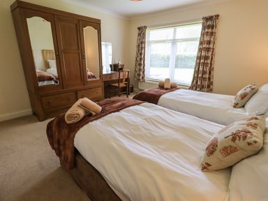 A bedroom with two single beds a wooden wardrobe and a dressing table by a window at Laal Field House in Keswick