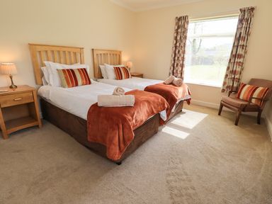 A bedroom with two single beds bedside tables with lamps a chair and a window with patterned curtains at Laal Field House in Keswick