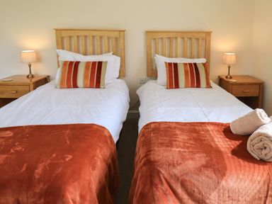 A bedroom with two single beds with striped pillows bedside tables and lamps at Laal Field House in Keswick