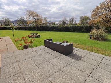 A patio with outdoor furniture and a round picnic table on a lawn with trees and bushes at Laal Field House in Keswick