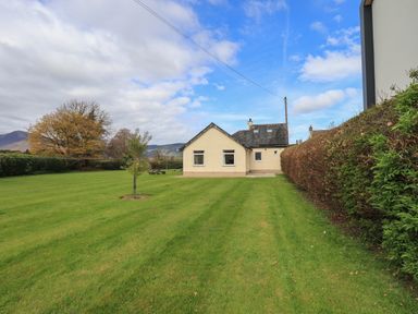 A house with a large lawn and small tree next to a hedge at Laal Field House in Keswick