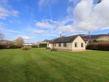 A single-story house with a lawn and outdoor seating surrounded by hedges and trees at Laal Field House in Keswick