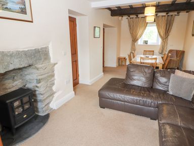 A living room with a brown leather sofa a stone fireplace and a dining table with chairs at Goswick Hall in Bowland Bridge