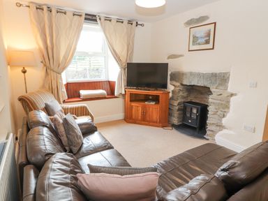 A living room with a leather sofa armchair lamp TV and stone fireplace at Goswick Hall Bowland Bridge