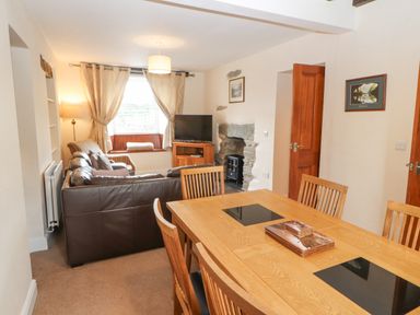 A dining table with chairs and a living area with sofas a television and a window at Goswick Hall in Bowland Bridge