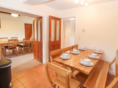 A dining area with a wooden table set with plates and glasses adjacent to another room with a larger wooden dining table and chairs at Goswick Hall in Bowland Bridge