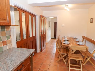 A dining area with a wooden table set with plates and glasses wooden chairs tiled floor and wooden doors at Goswick Hall in Bowland Bridge