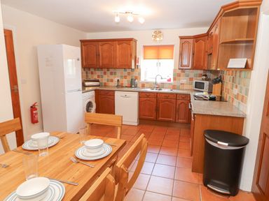 A kitchen with wooden cabinets a dining table set with plates bowls and glasses and kitchen appliances at Goswick Hall in Bowland Bridge