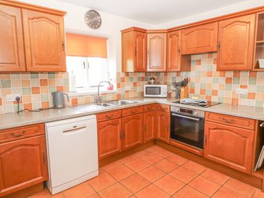 A kitchen with wooden cabinets a dishwasher a microwave a sink and a stove at Goswick Hall in Bowland Bridge
