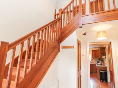A wooden staircase in a hallway next to a doorway leading to a kitchen at Goswick Hall in Bowland Bridge