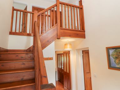 A wooden staircase with a railing and doors under the landing at Goswick Hall in Bowland Bridge