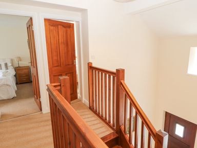 A hallway with wooden staircase and doors leading to bedroom at Goswick Hall in Bowland Bridge