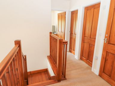 A hallway with wooden doors and wooden stair railing at Goswick Hall in Bowland Bridge