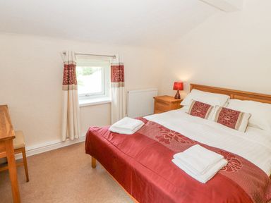 A bedroom with a double bed bedside table lamp window and wooden desk at Goswick Hall in Bowland Bridge