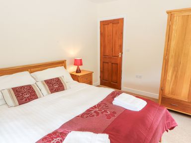 A bedroom with a double bed bedside table with lamp wooden wardrobe and closed wooden door at Goswick Hall in Bowland Bridge