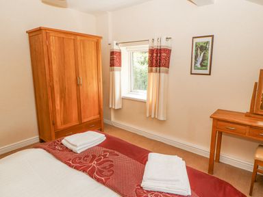 A bedroom with a wooden wardrobe a wooden dressing table a window with curtains and a bed with towels at Goswick Hall in Bowland Bridge