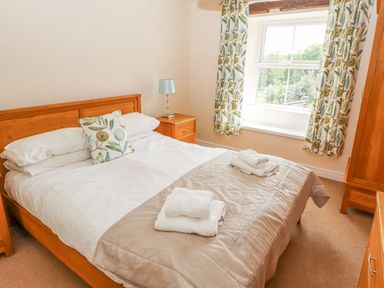 A bedroom with a double bed white sheets folded towels on bed floral curtains and wooden furniture at Goswick Hall in Bowland Bridge
