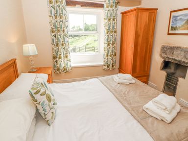 A bedroom with a bed pillows bedside table lamp wardrobe and window with patterned curtains at Goswick Hall in Bowland Bridge