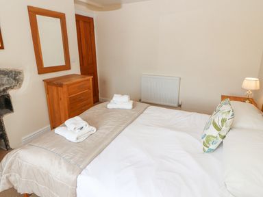 A bedroom with a made bed towels on bed a wooden dresser mirror radiator and a lamp at Goswick Hall in Bowland Bridge