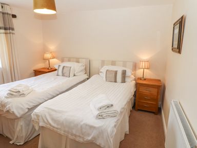 A bedroom with two single beds bedside tables with lamps and folded towels at Goswick Hall in Bowland Bridge